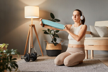 Athlete attractive woman wearing beige sportswear and headphones exercising with resistance band...