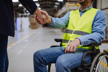 Portrait of man in wheelchair working in warehouse, shaking hand with HR manager, director. Concept of workers with disabilities, accessible workplace for employees with mobility impairment.