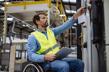 Portrait of man in wheelchair working in modern industrial factory, in adjustable workstation....