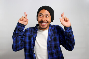 Excited young Asian man, dressed in a beanie hat and casual shirt, expresses enthusiasm by making a...