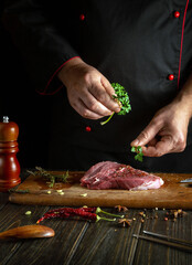 The cook adds aromatic parsley to the meat steak for a delicious taste. The concept of cooking veal shish kebab on the kitchen table.