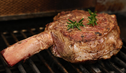 A single ribeye steak on the bone with rosemary herb garnish  in the early stages of cooking on the...