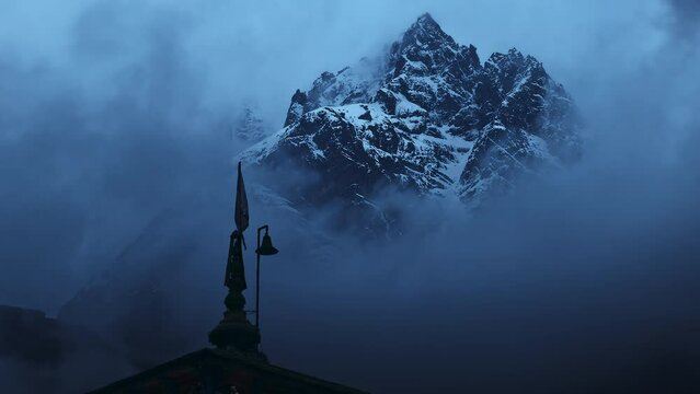 A beautiful shot of the cloudy and snowy Himalayan mountains behind the Kedarnath temple in Uttarakhand, India.