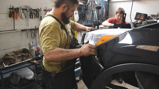 Two mechanics removing front bumper from car for repair in auto service. Professional repairmans dismantling automobile before fix at workshop or garage. Concept of vehicle maintenance and diagnostic