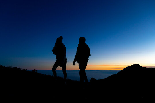 Silhouette of unrecognizable traveler couple admiring orange sunset on highland