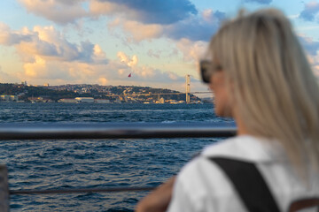 Young female traveler in a white shirt and with a craft backpack enjoys a magnificent view of the Bosphorus and the European part in Istanbul, selective focus.