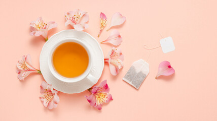 Cup of tea with flowers and tea bag with white empty label on pink background, top view, banner size. Fruit natural aroma tea with teabag