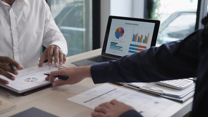 Asian businessman conversing with a team colleague, presenting and discussing a project via laptop. Engaged in purposeful work within a modern office setting. Professional collaboration.