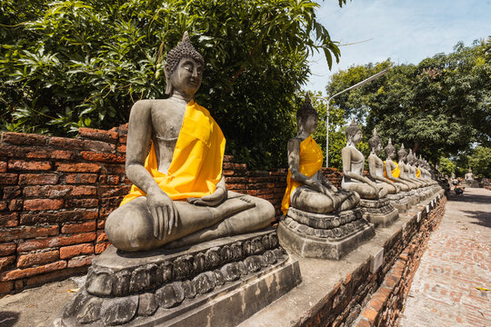 Sitting Buddha statues in ancient temple yard with green trees in daylight in Thailand