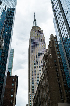 Modern skyscrapers and Empire State building in city under cloudy sky