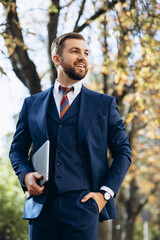 Business man in suit holding laptop and walking in the street