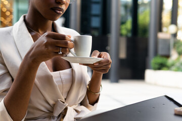 Unrecognizable black businesswoman drinking coffee while sitting at table