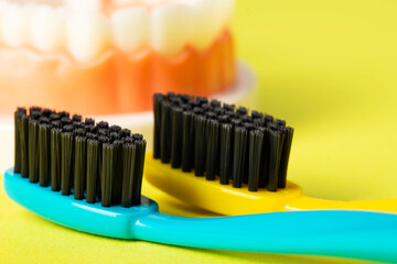 Two toothbrushes with black charcoal hard bristles on a yellow background, close-up. The concept of...