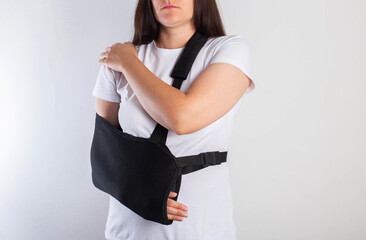 A girl on a white background with a black supporting medical bandage after a dislocation of the...