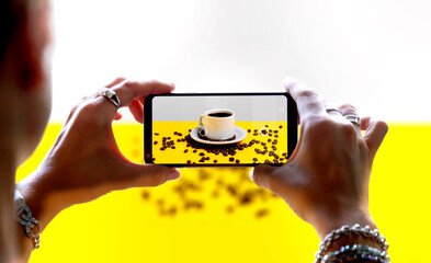 Woman using a smartphone camera to take a photo of a coffee. While shooting, it is displayed on the mobile camera screen. Product photography concept.
