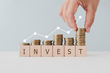 INVEST text on wooden cubes block under stack of coin and graph. For Financial investment growth or...