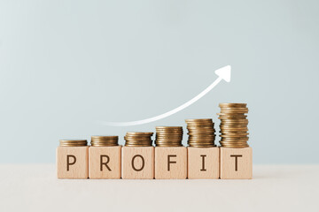 PROFIT text on wooden cube blocks with stack of coin above and increasing graph. For financial...