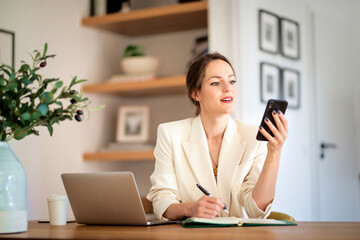Confident woman sitting at home and using laptop and smartphone for work