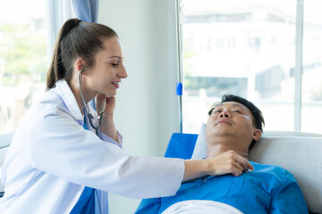 An Asian male patient lies in a hospital bed and is carefully looked after by a doctor. Doctor...