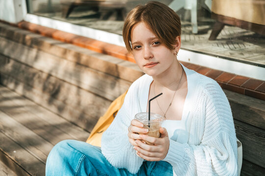 A trendy teenage girl, exuding cool vibes, leisurely sips on iced coffee
