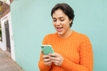 Cheerful woman using smartphone against turquoise wall in city