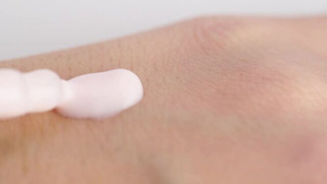 Moisturizing serum lotion in peach fuzz colour in pipette falling at the woman's hand, skin care cosmetics. Pastel light pink drop of essence on the dry skin. Macro