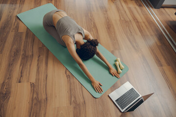 Active fit woman doing stretching exercise on mat in living room at home while use laptop