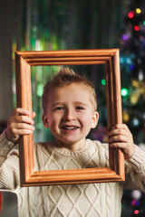 portrait of a cute boy of European appearance in a wooden picture frame against the backdrop of a Christmas tree in the room