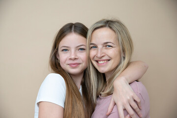 beautiful young, teenager girl together with her beautiful mother posing in front of brown background