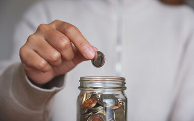 Closeup image of a woman collecting and putting coins in a glass jar for saving money concept