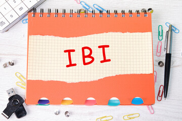 IBI word is written on a sheet in a cage lying on a notebook on the table next to stationery