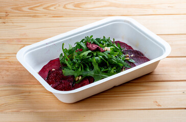 Beet carpaccio, arugula and nuts. Vegetarian food. Takeaway food. On a wooden background.