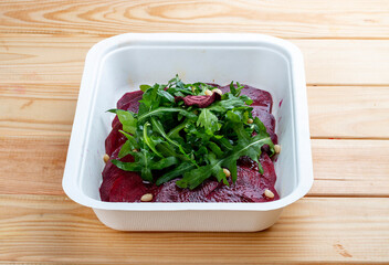 Beet carpaccio, arugula and nuts. Vegetarian food. Takeaway food. On a wooden background.