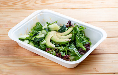Salad with greens and avocado. Vegetarian food. Takeaway food. On a wooden background.