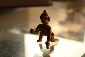 A shiny brass figurine of laddu Gopal or lord Krishna on a glass surface with background blur,...