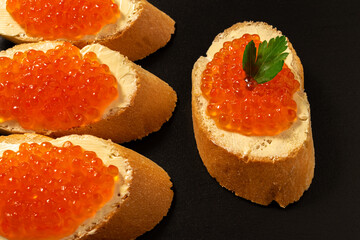 Sandwiches with salmon red caviar on a dark stone background.