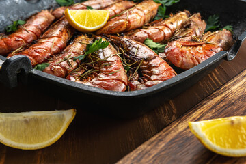 Fried shrimps on grill pan with fresh herbs and lemon slice. Seafood background.