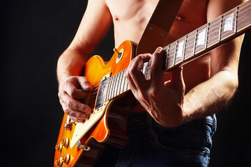 Artist plays the orange sunburst electric guitar on dark stage. - obrazy, fototapety, plakaty