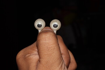 Googly eyes ring in the thumb of a person with isolated black background, eyes upward