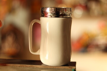 A large White Mug cup with silver lid cap on it on a glass surface 