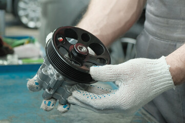 The power steering pump.Close-up.An auto mechanic checks the serviceability and compliance of a spare part before replacing it during car repair at a service station.