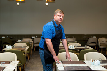A man clears a table in a cafe end of the working day.