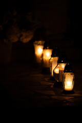 Night shot of the flames of glass cemetery candles standing on tombstones. The shot was taken during All Saints' Day, November 1.
