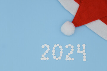 White medical pills in form of number 2024 and Santa hat on blue background. Christmas medical flat lay.