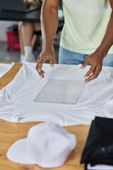 Obraz na płótnie Canvas partial view of african american designer holding transparent format template near white t-shirt