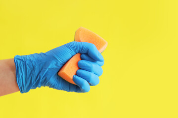 Sponge in hand, wet cleaning of the room, bright yellow background. A woman's hand in a latex blue glove with an orange sponge. Cleaning. Wash dishes - obrazy, fototapety, plakaty