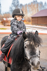 Little cute girl riding a little horse or pony in the winter in field in the winter