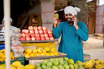 Young Indian fruit seller showing or talking phone at the camera, mixing tradition with technology.