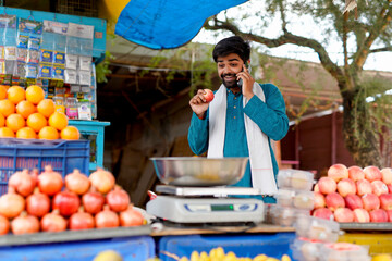 Young Indian fruit seller showing or talking phone at the camera, mixing tradition with technology.