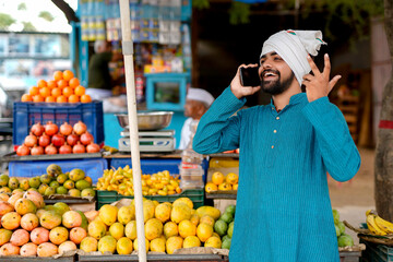 Young Indian fruit seller showing or talking phone at the camera, mixing tradition with technology.